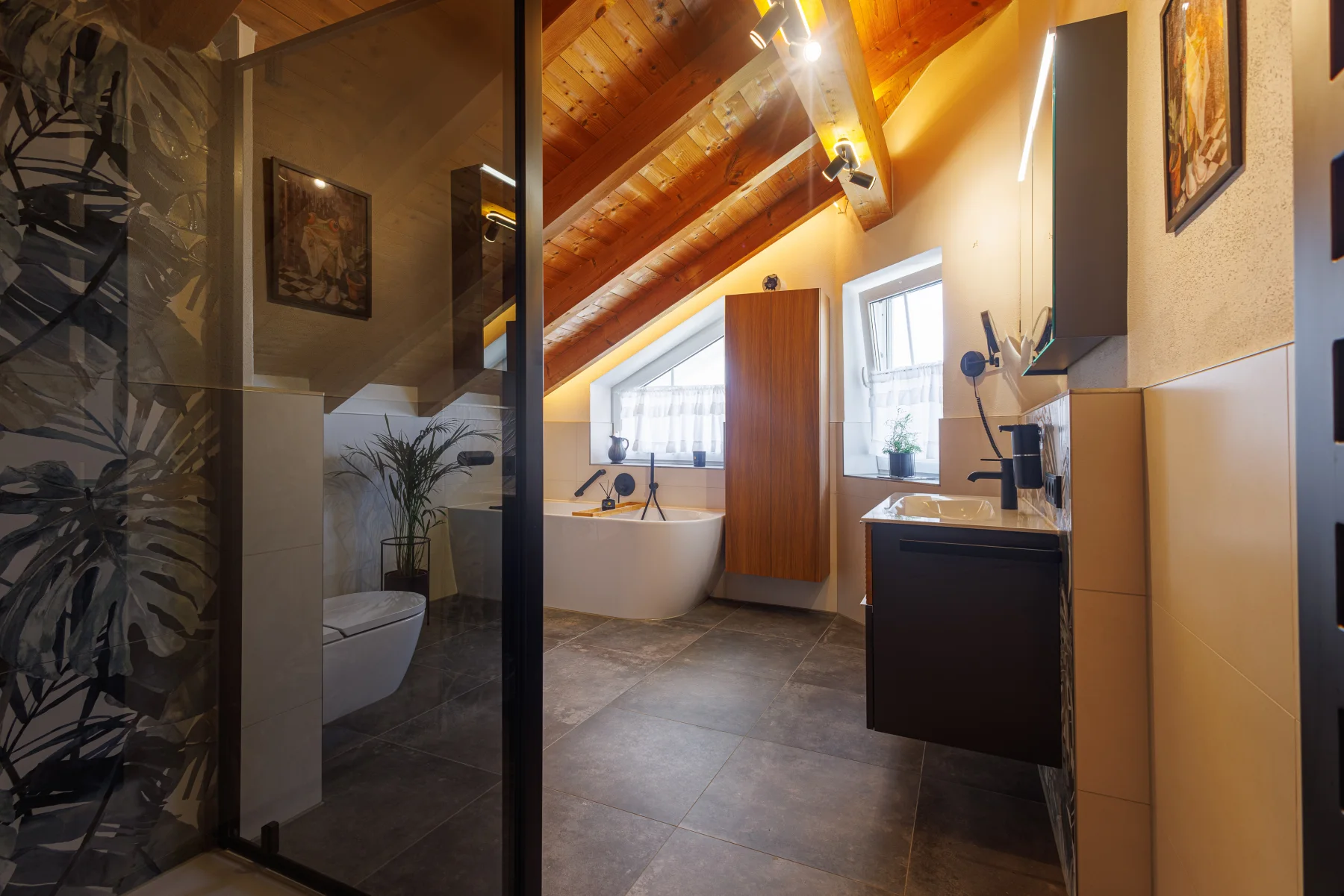 Blick über den Waschtisch zur Dusche hinter Glas, dahinter die Badewanne unter der Dachschräge
