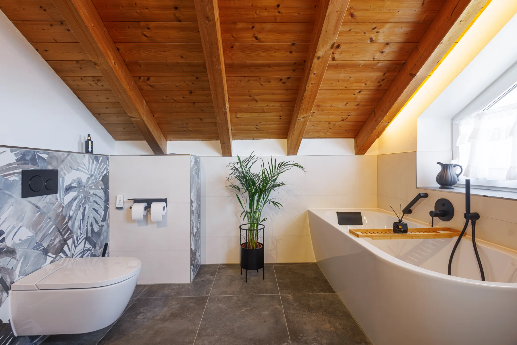 Eckbadewanne mit schwarzer Armatur und Holzablage unter einer Dachschräge, daneben ein wandhängendes WC