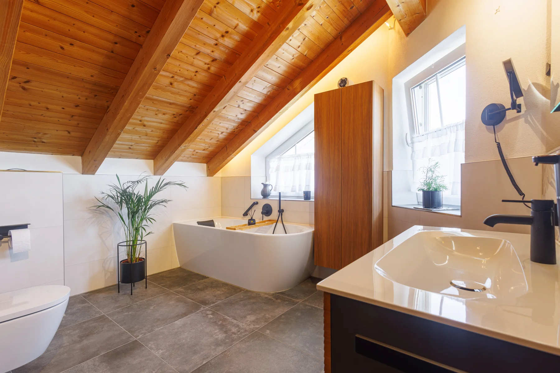 Gesamtansicht des Bades mit Holzdecke, Waschtisch, Wanne und Grünpflanze