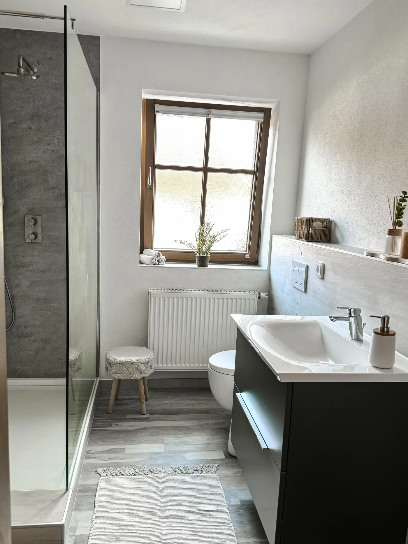 Saniertes Bad mit bodengleicher Dusche in Betonoptik und Holzfenster