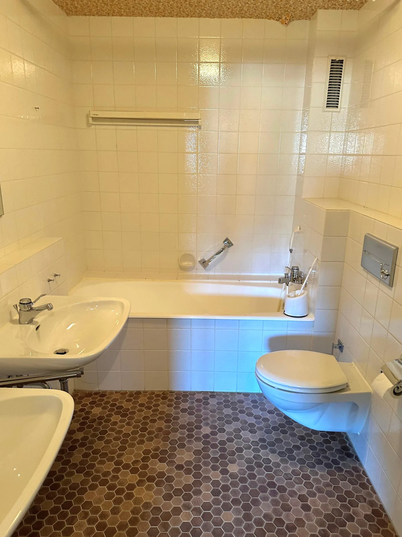Altes Bad mit weißen Wandfliesen, Badewanne und braunem Sechseckboden
